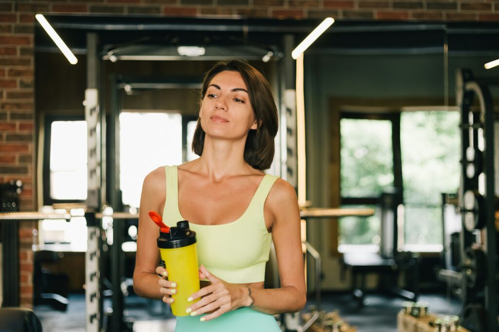 Fit caucasian beautiful woman in fitting sport wear at gym holds protein shaker